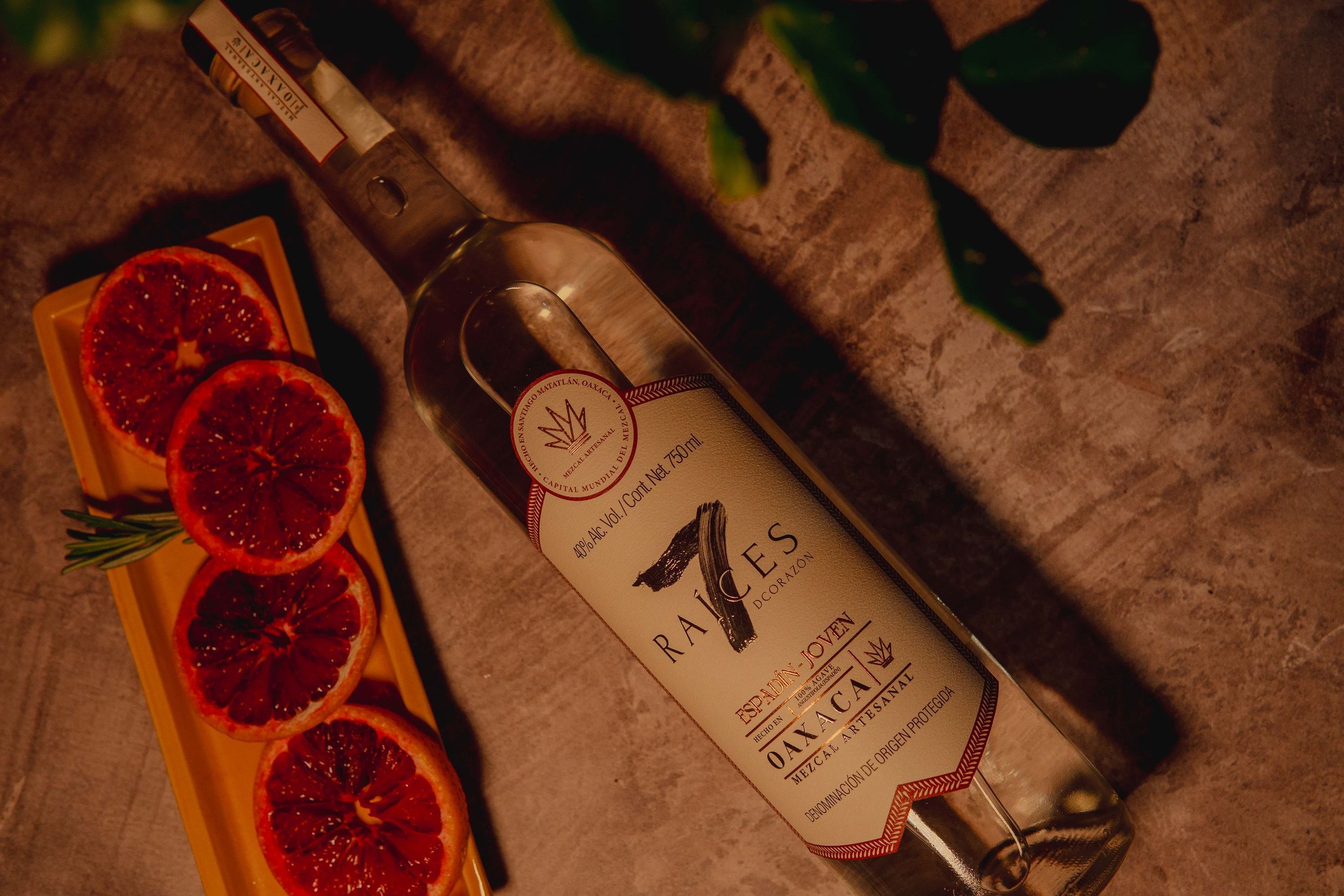 Botella de mezcal 7 Raíces espadín junto a rodajas de naranja sobre una tabla de madera